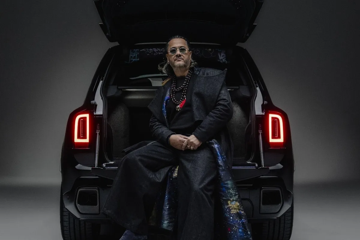 Cyril Kongo sitting on the open tailgate of a black Rolls-Royce Black Badge Cullinan in studio.