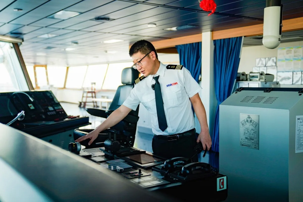 Uniformed ship officer operating controls on the bridge of a cargo vessel