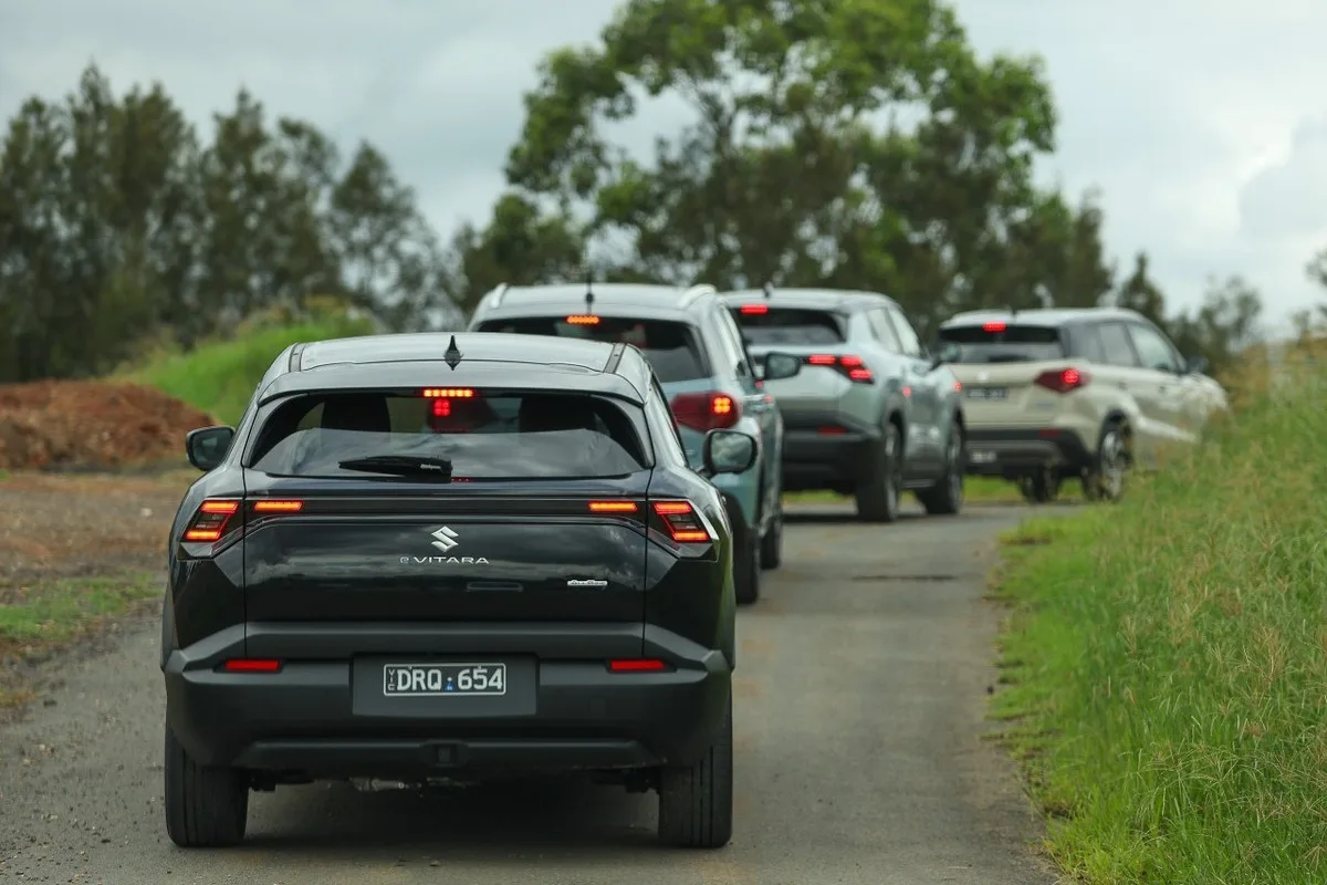 Rear view of several Suzuki e VITARA SUVs driving in a line on a rural road.