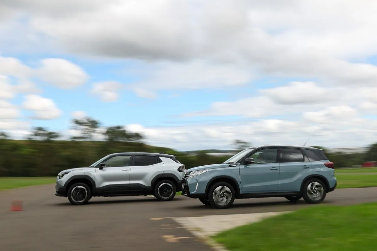 Silver and blue-grey Suzuki e VITARA SUVs driving side by side on a road.