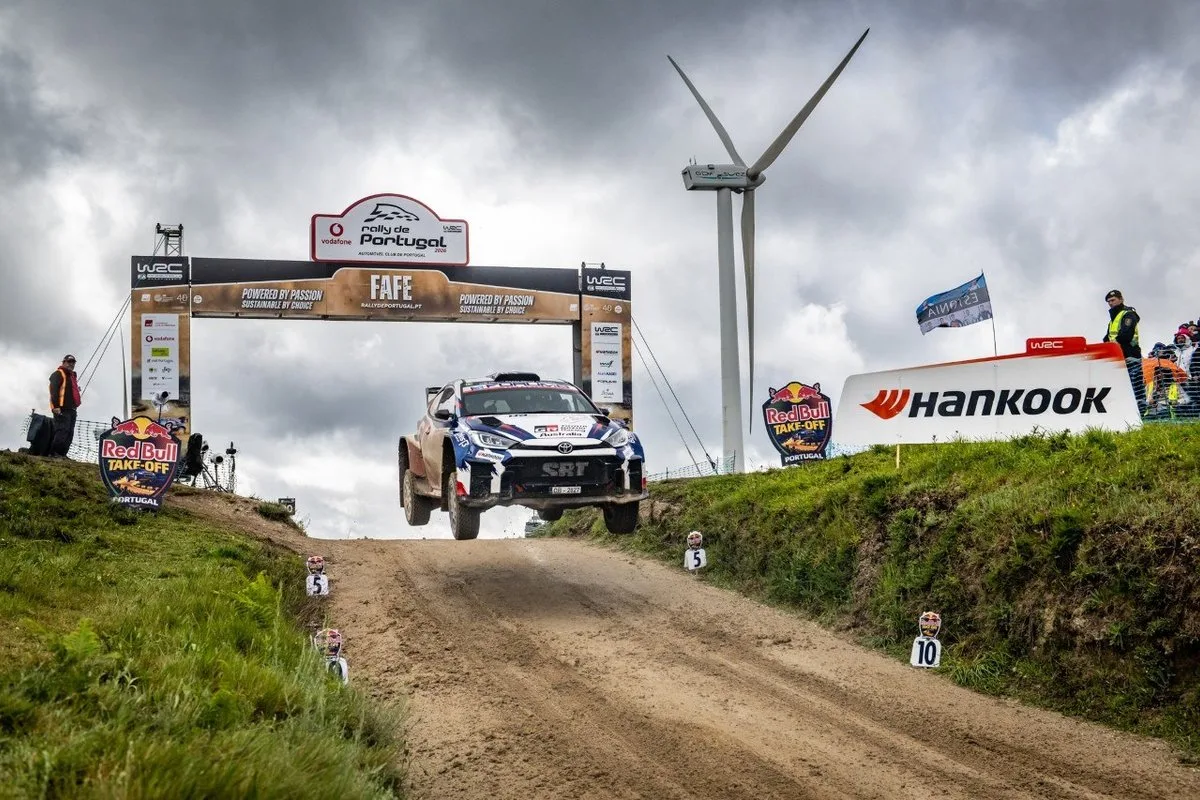 Toyota GR Yaris rally car jumping over a gravel crest at Rally de Portugal with spectators and WRC signage.