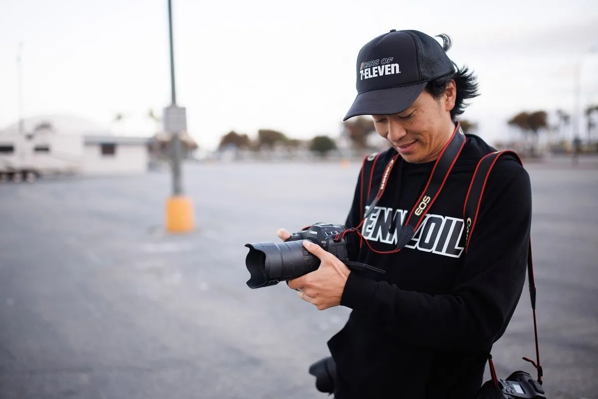 Automotive photographer Larry Chen with camera gear at an outdoor car event.
