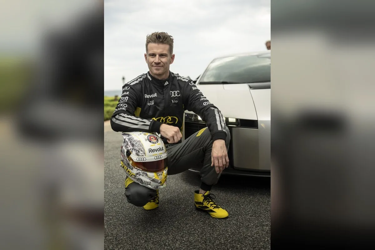Nico Hulkenberg crouching beside the front of the Audi Nuvolari with his helmet