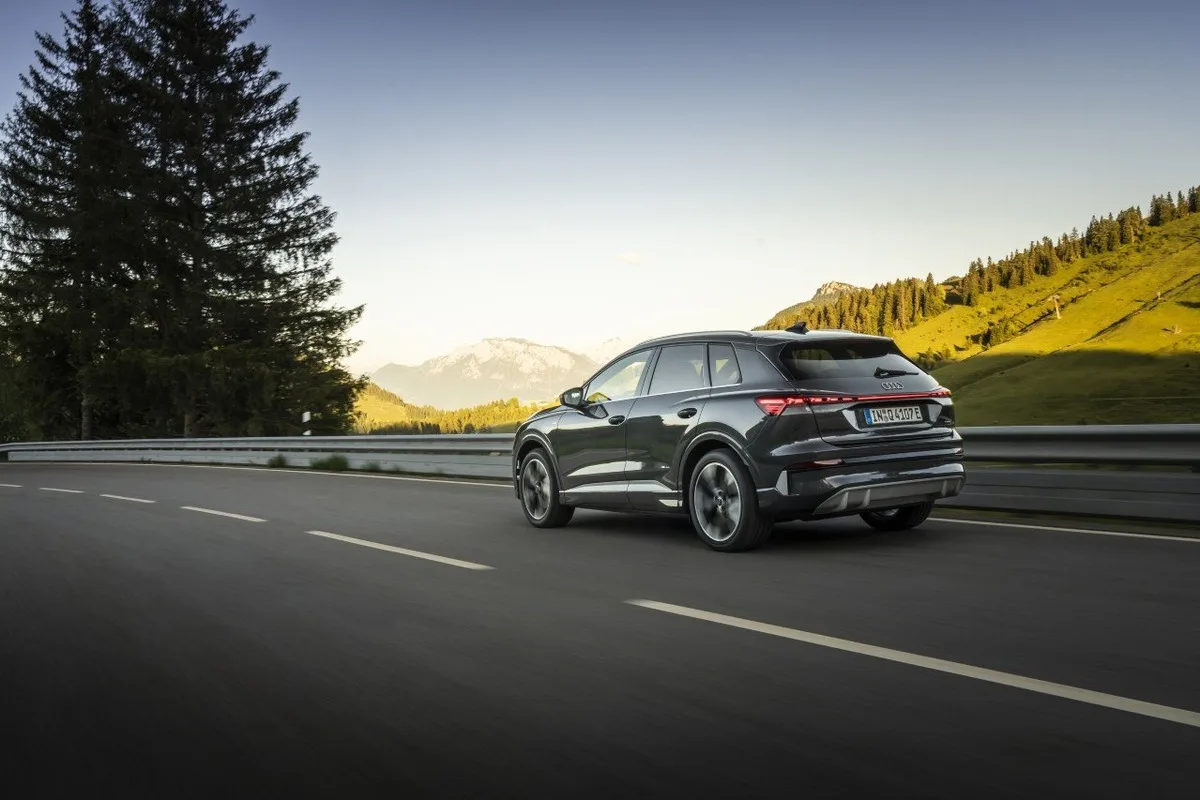 Black Audi Q4 e-tron SUV driving through Alpine scenery at sunset.