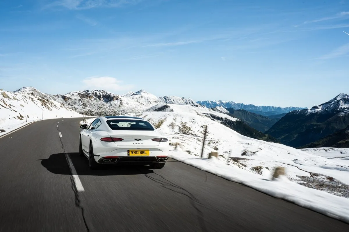 White Bentley Continental GT driving along the Grossglockner High Alpine Road in snow-covered mountains