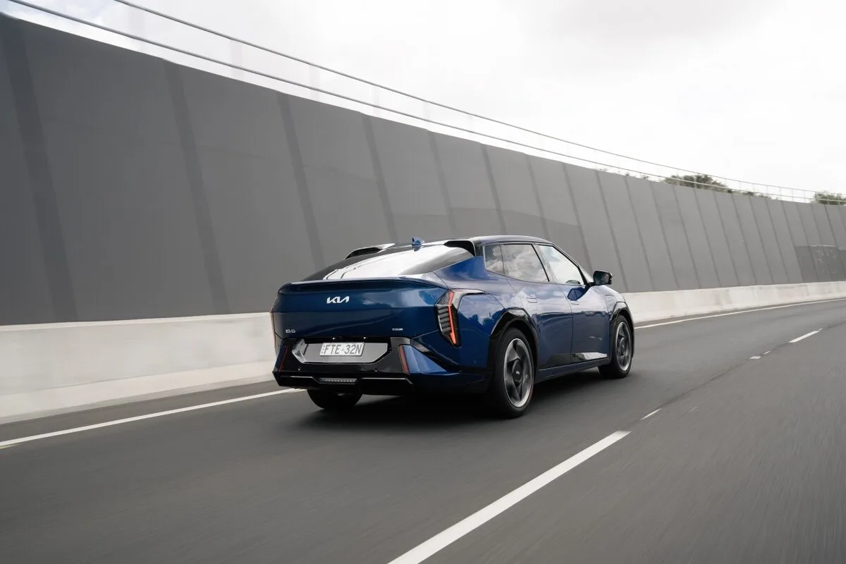 Blue 2026 Kia EV4 Earth Long Range rear three-quarter view driving on a city motorway