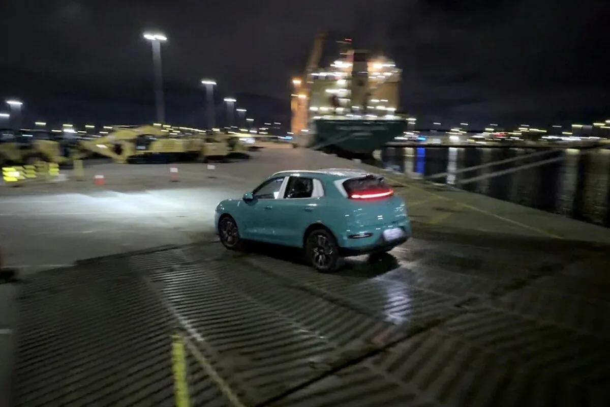 Turquoise ORA 5 SUV driving away from a ship at a port at night