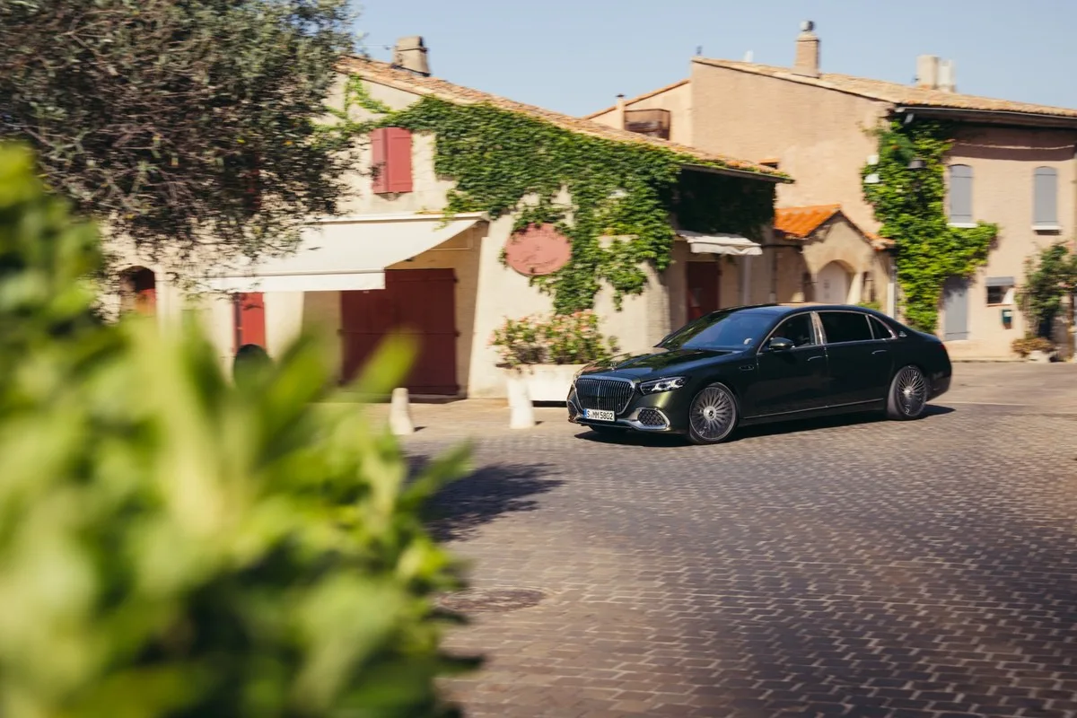Dark green Mercedes-Maybach S-Class driving past an ivy-covered building in a village in Provence
