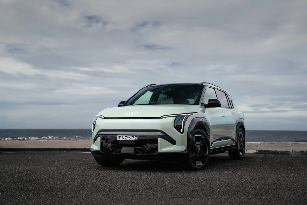 Light green Kia EV3 GT-Line electric SUV parked front-on beside a sea wall with the ocean behind under a grey sky