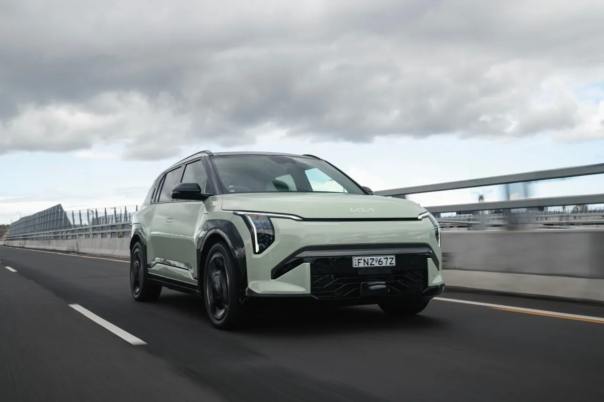 Light green Kia EV3 GT-Line electric SUV driving along a motorway past a safety barrier under cloudy skies