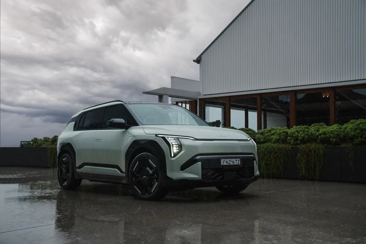 Light green Kia EV3 GT-Line electric SUV parked on wet ground beside a modern building during light rain