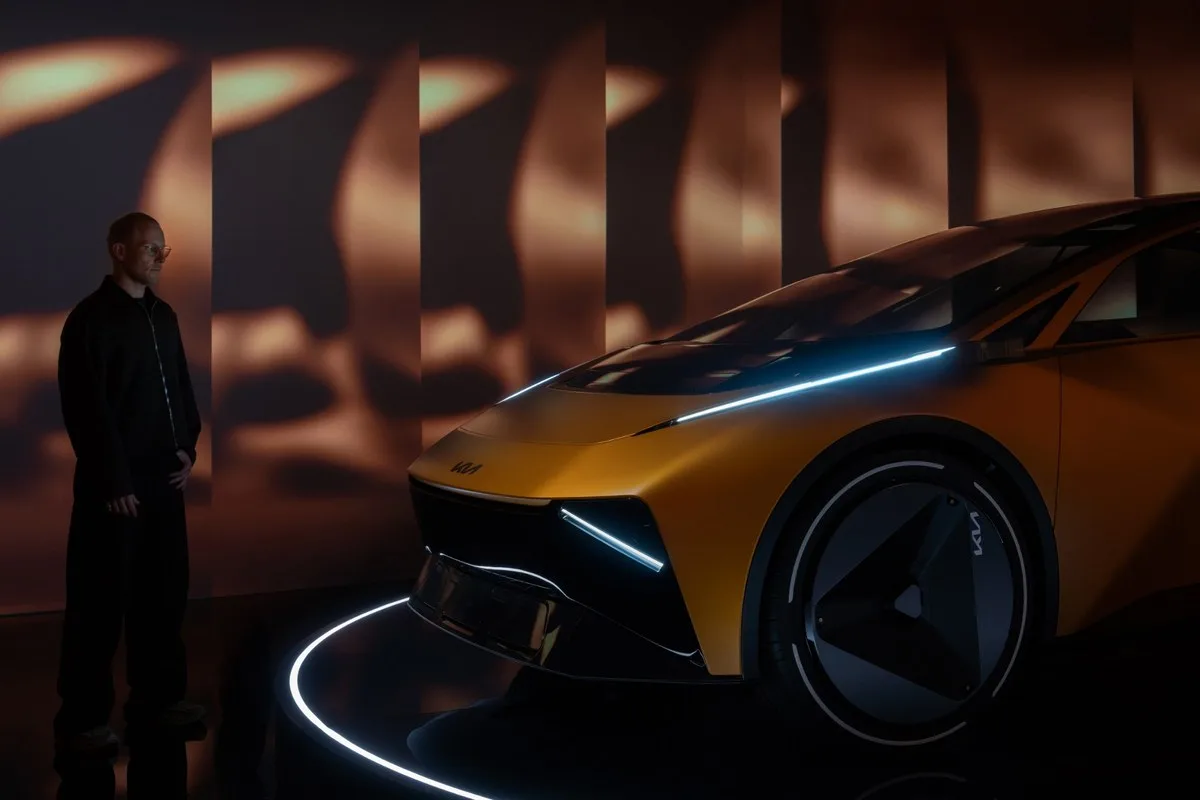 A designer stands beside the gold Kia Vision Meta Turismo in a darkened studio lit by a glowing light bar