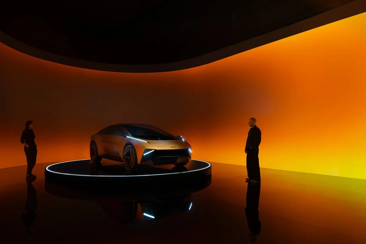 Kia Vision Meta Turismo on a lit turntable flanked by two people in an orange-lit studio
