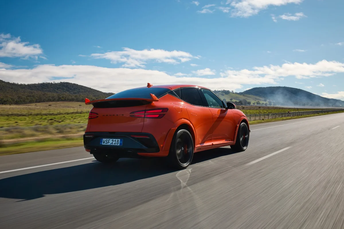 Magma Orange Genesis GV60 Magma driving away on a country road, rear three-quarter