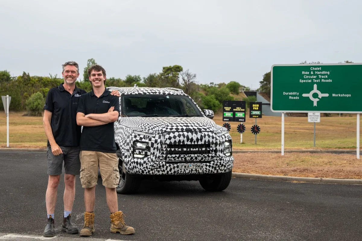 Camouflaged JAC Hunter dual-cab ute parked at a vehicle proving ground with two engineers standing beside it