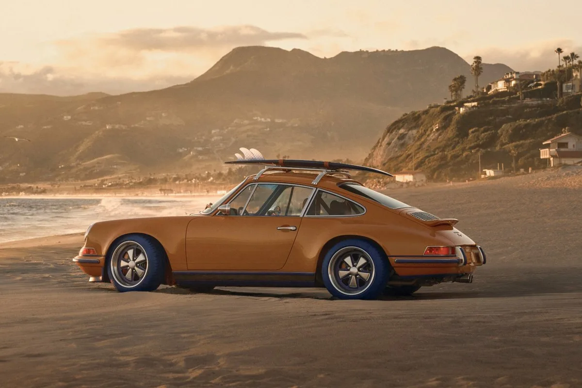 Saffron Porsche 911 Reimagined by Singer Classic with a surfboard on the roof rack