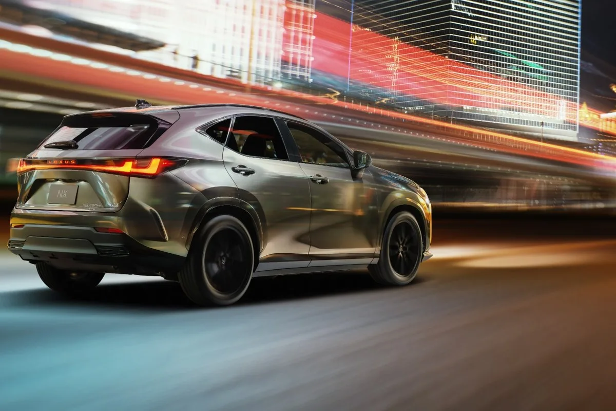 Rear three-quarter view of a silver 2027 Lexus NX 450h+ AWD on a city street at night