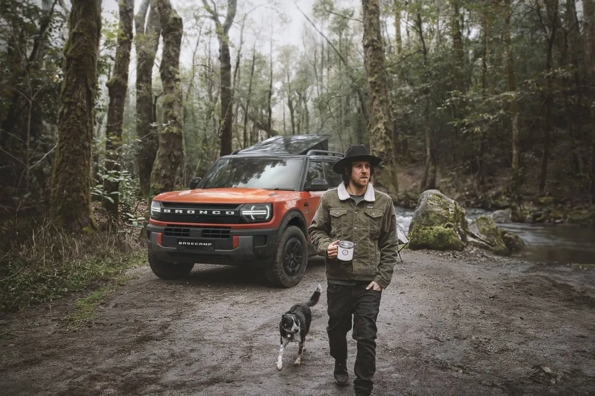Orange Ford Bronco Basecamp parked on a forest track with a man and a dog walking past