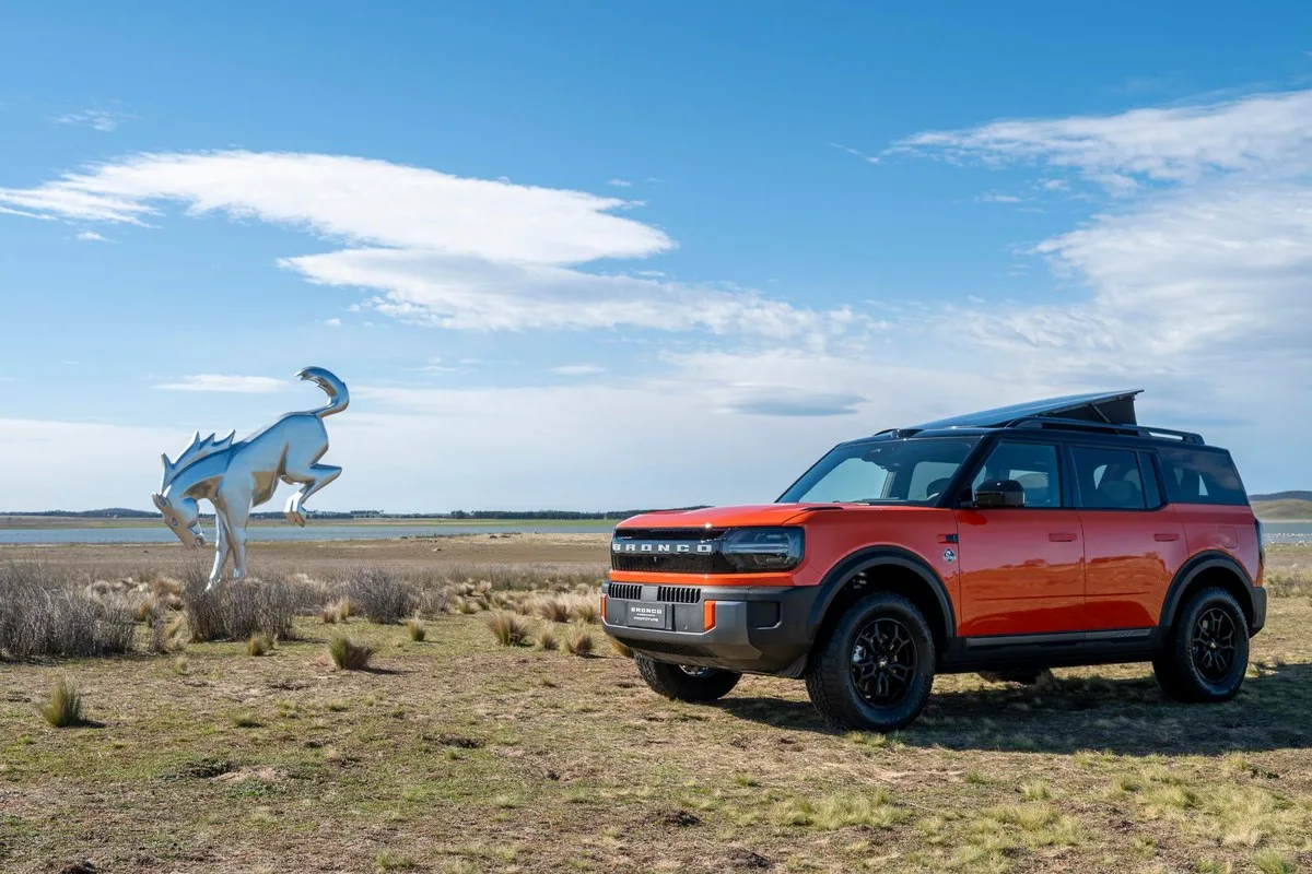 Orange Ford Bronco Basecamp parked in grassland beside a large chrome bucking horse sculpture