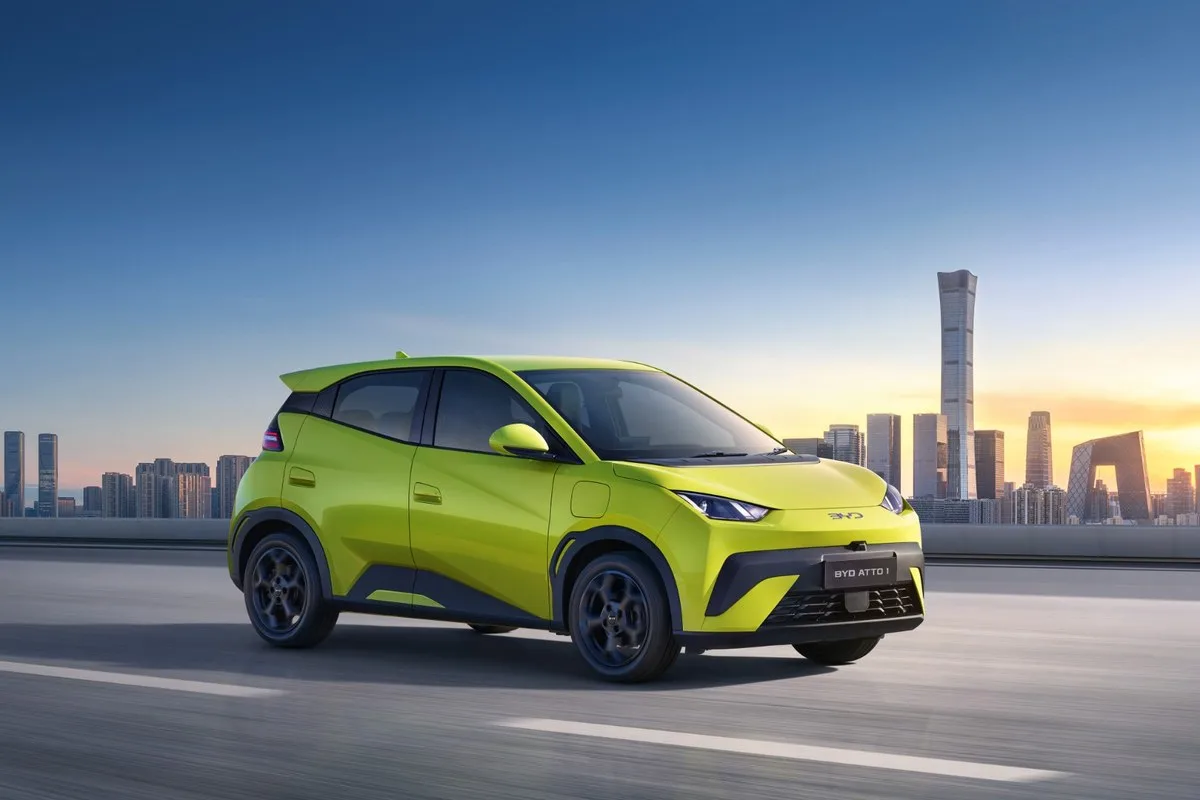 BYD ATTO 1 in lime green driving, side profile, city skyline behind.