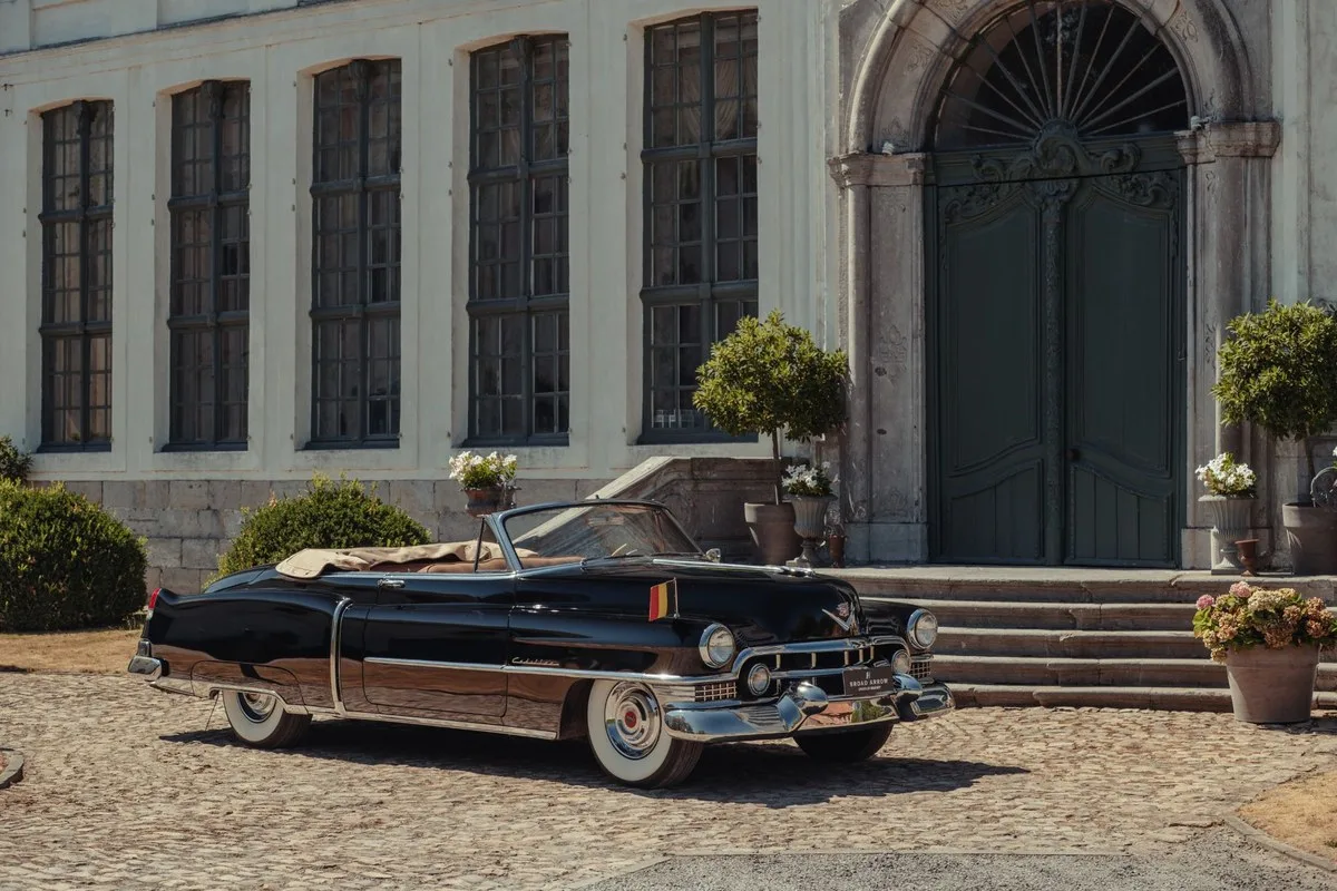 Black 1951 Cadillac Series 62 Convertible with a Belgian flag outside a chateau