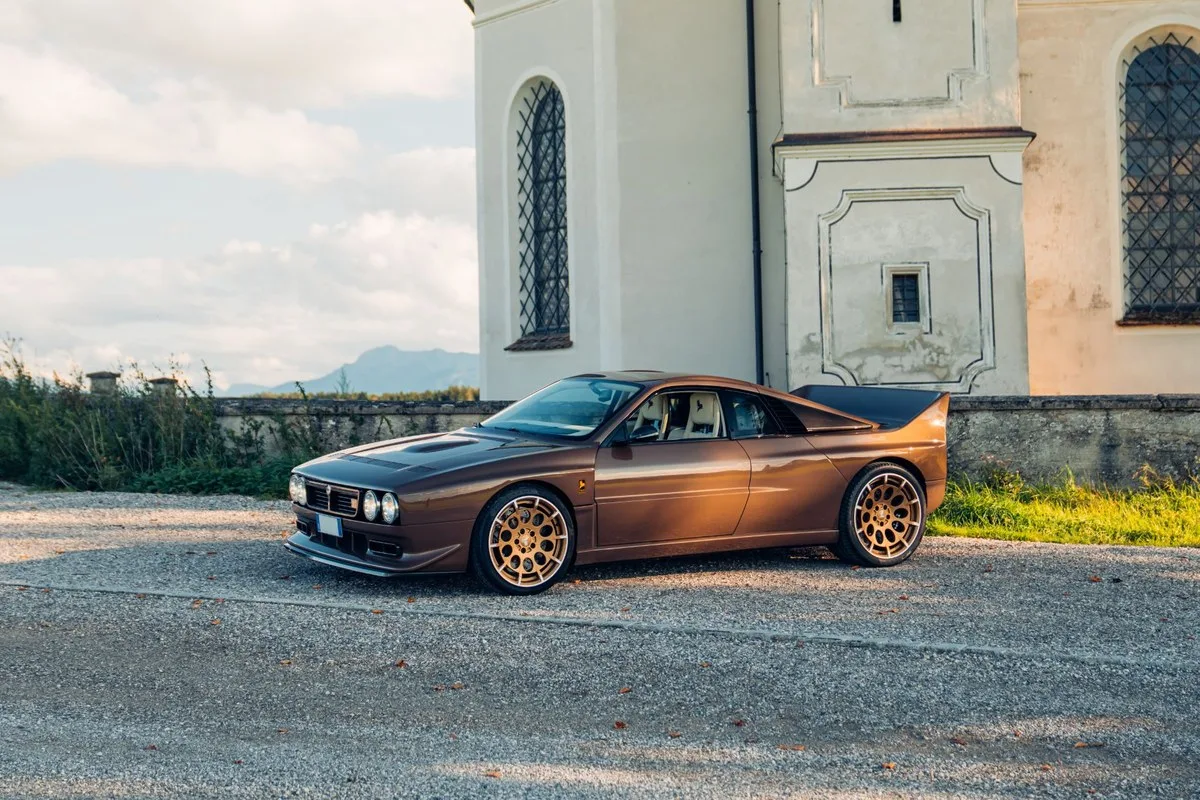 Brown Lancia Kimera EVO37 with gold wheels outside a white church