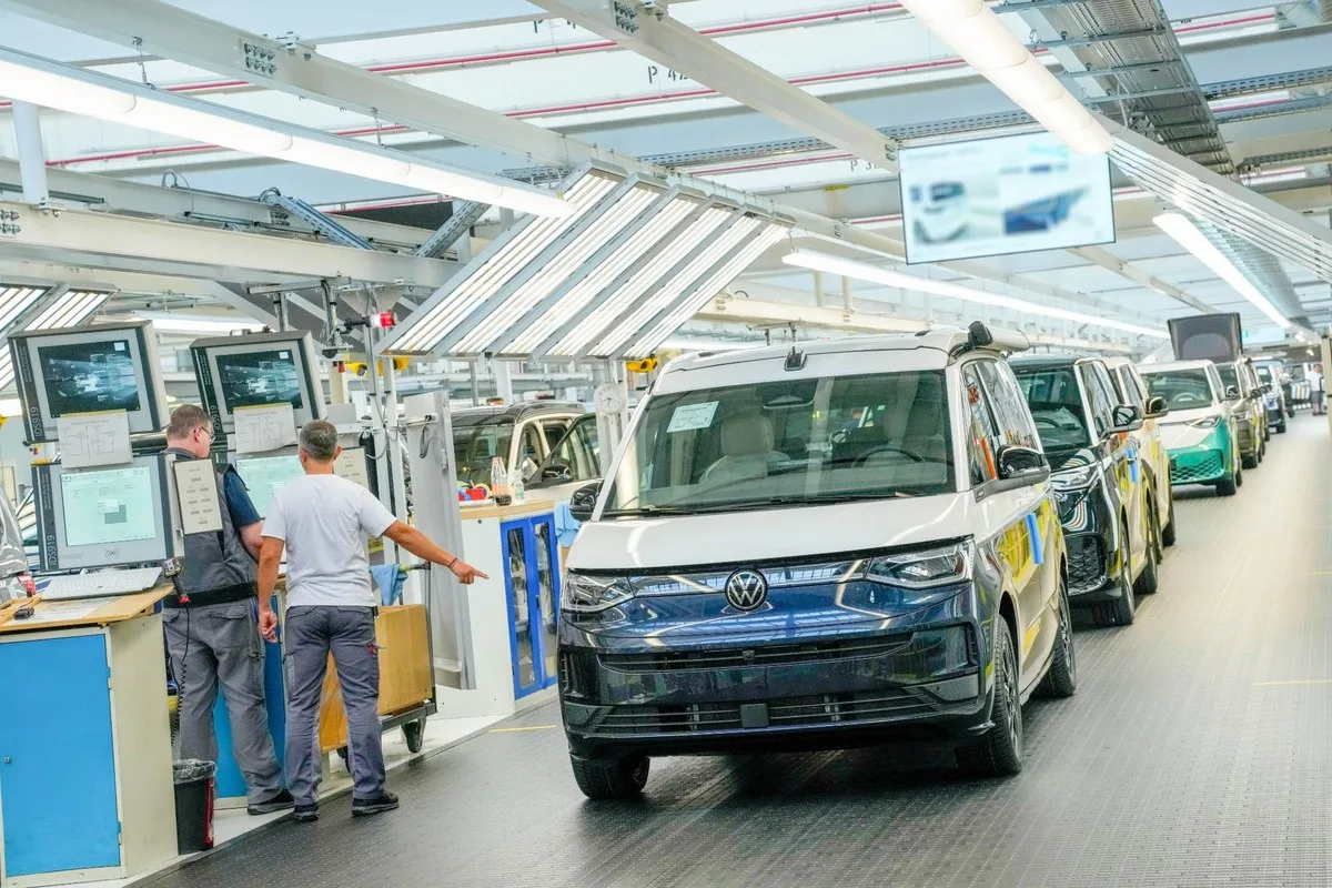 White Volkswagen Caravelle on the assembly line with two workers alongside