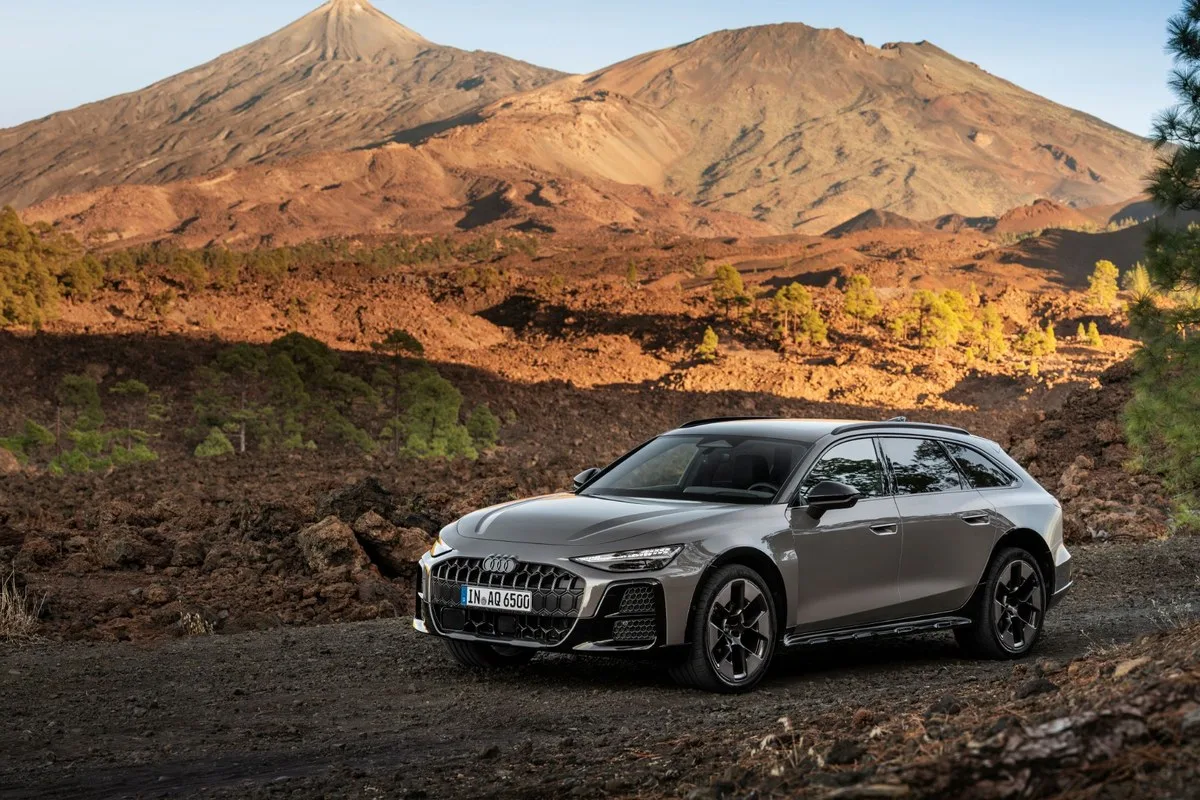 Grey Audi A6 allroad parked on a gravel track below a volcano