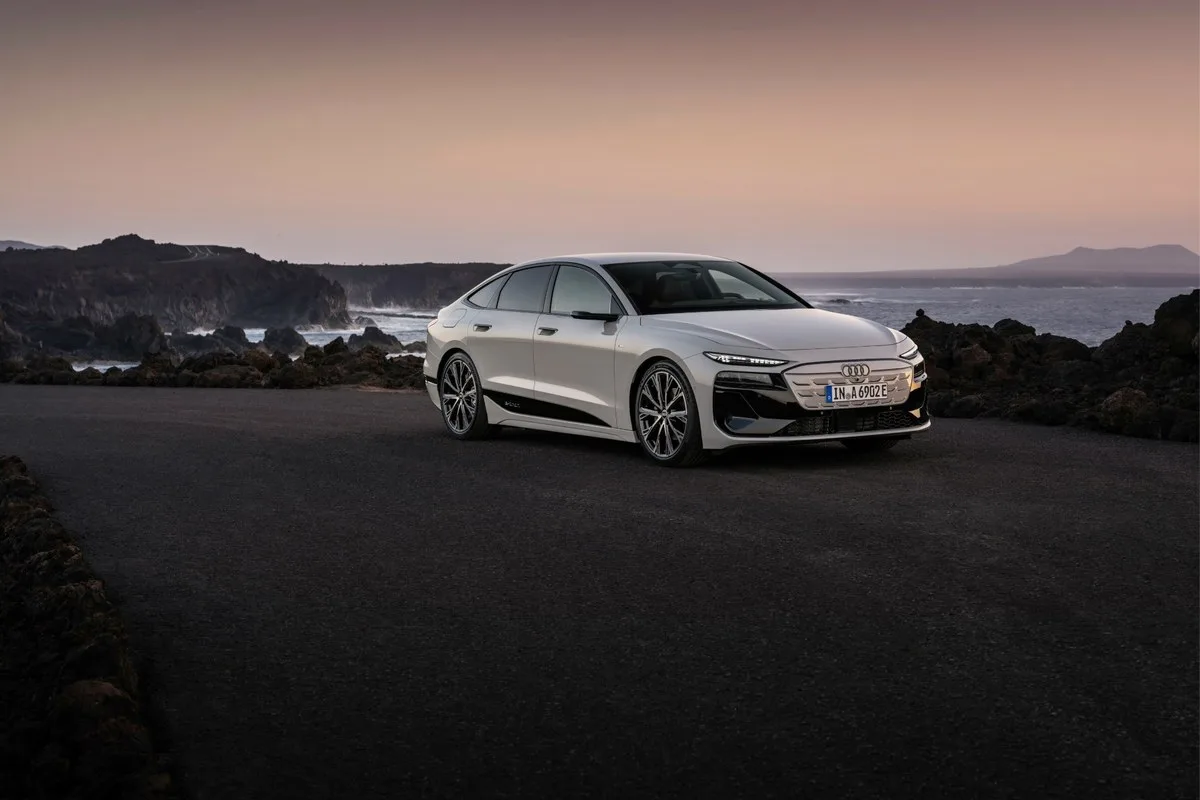 White Audi A6 Sportback e-tron front three-quarter view on a coastal road at dusk