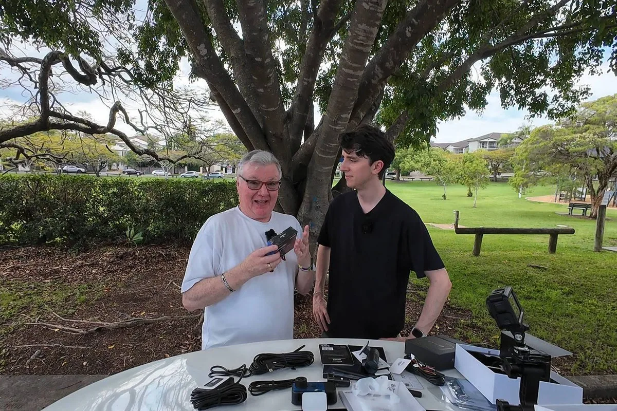 Alan Zurvas holding a gadget box beside a co-host at a park table