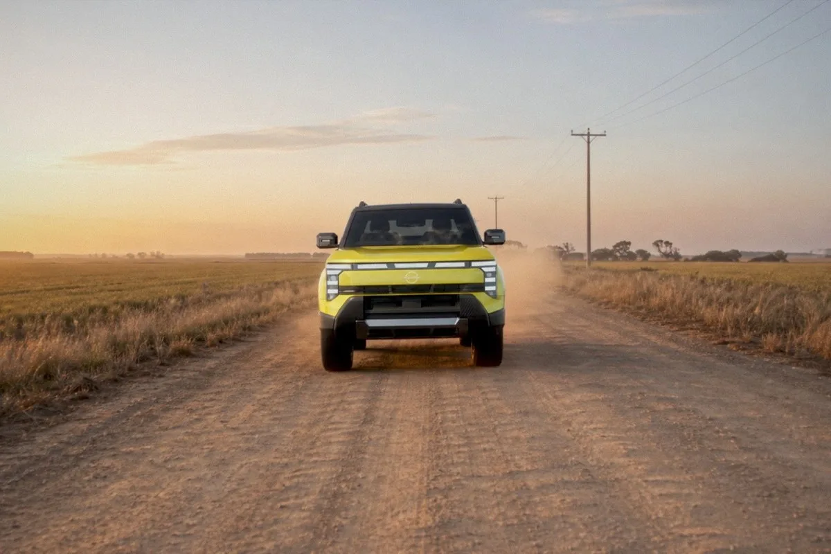 Yellow Nissan Navara Pro PHEV driving head-on along a dusty country dirt road at sunset