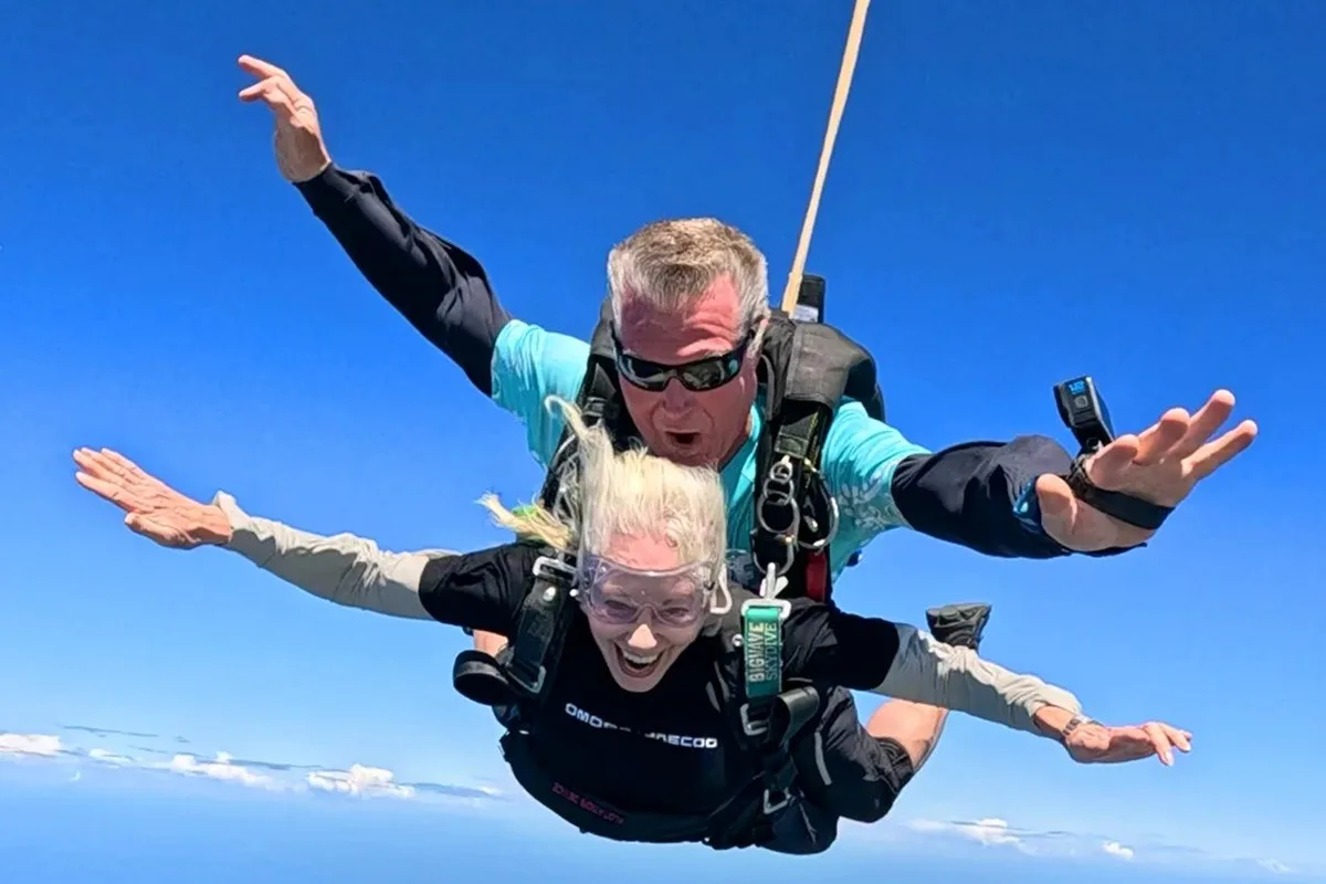 Grandmother and tandem instructor in freefall with arms spread against a blue sky