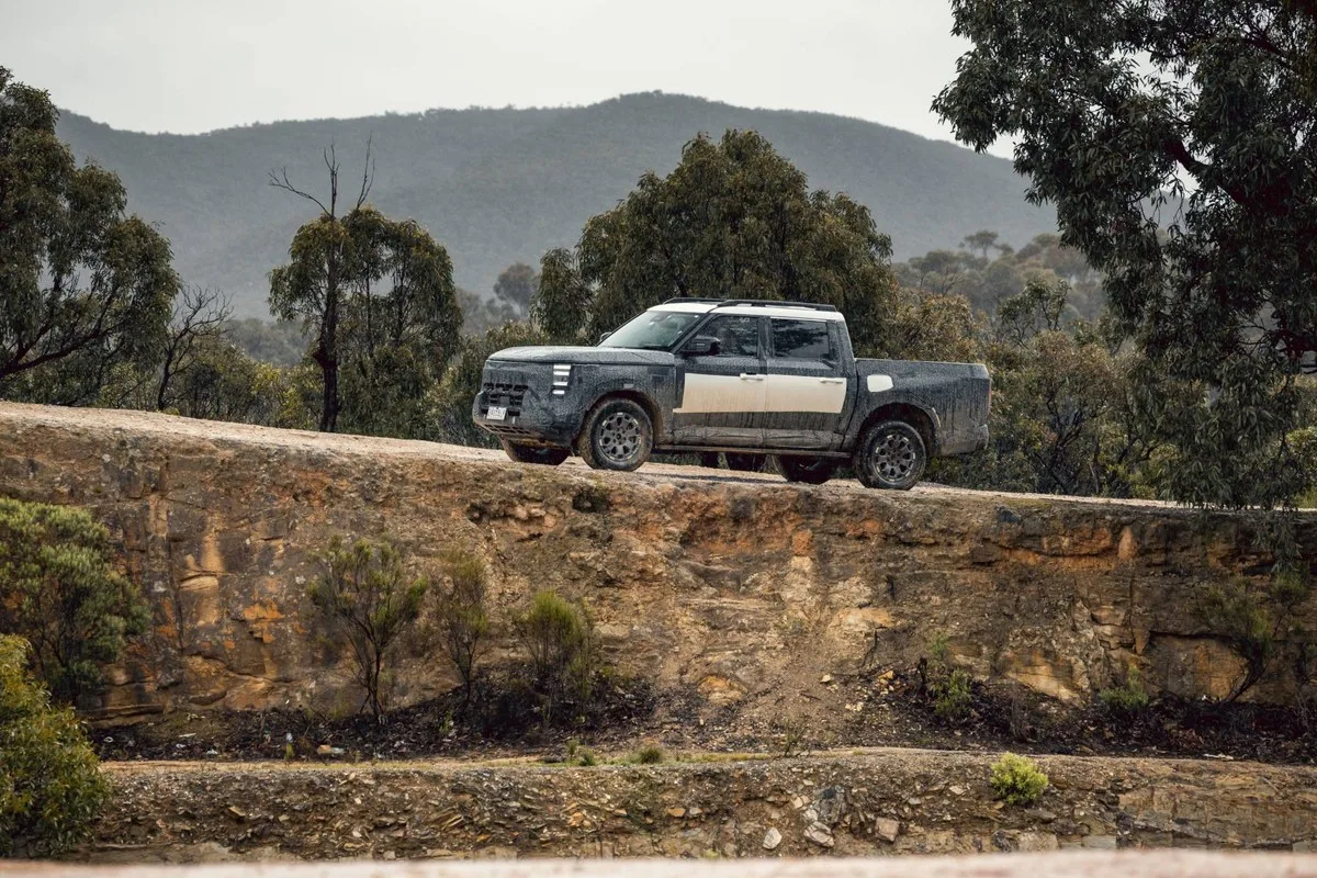 Camouflaged Nissan Navara Pro PHEV prototype dual-cab ute driving along a rocky ridge track in the Australian bush