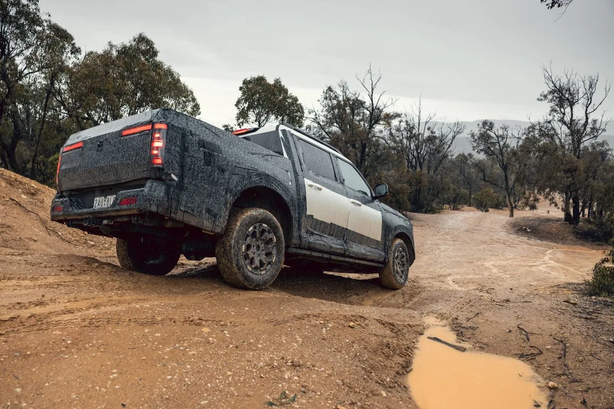 Camouflaged Nissan Navara Pro PHEV prototype on a muddy dirt track, rear three-quarter view with LED tail lights