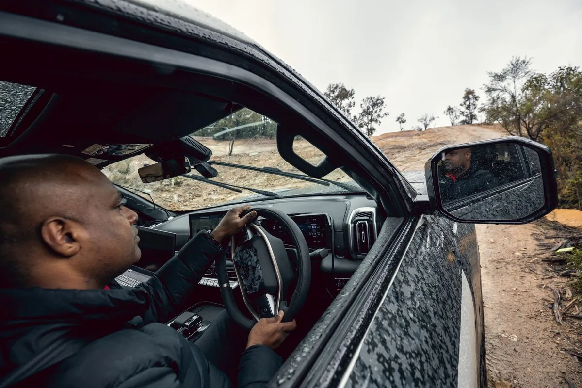 Driver at the wheel of the Nissan Navara Pro PHEV prototype on a dirt track, with touchscreen and digital instruments visible