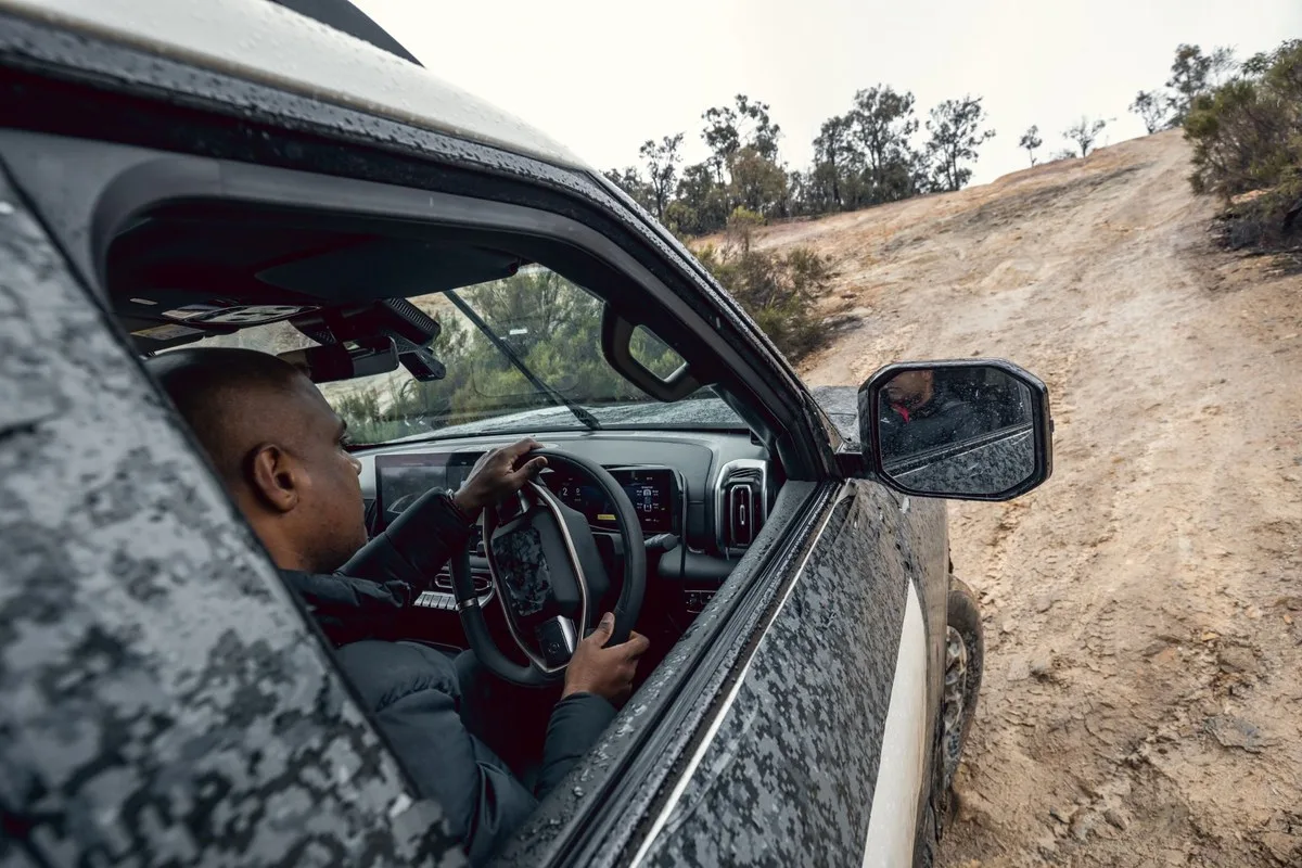 Driver steering the camouflaged Nissan Navara Pro PHEV prototype up a steep dirt hill