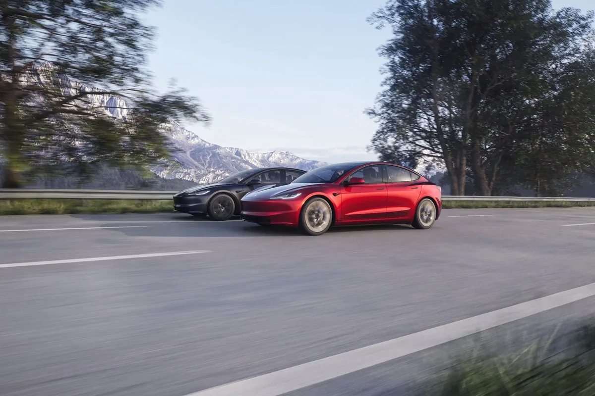 Red and black Tesla Model 3 sedans driving on a mountain road